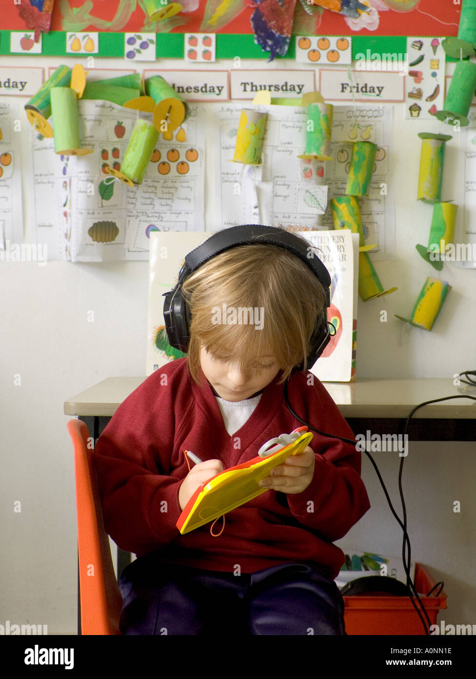AUDIO-UNTERRICHT Kleinkind 3-5 Jahre Kind Spielschule Kindergarten Mädchen Schüler schreibt auf Pad, während Audio-Beschreibung über Kopfhörer hören Stockfoto