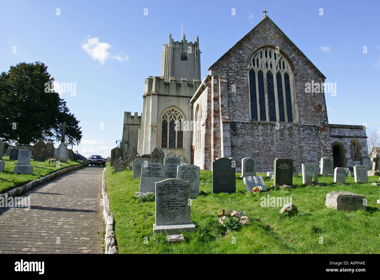 Traditionelle britische Kirche steht auf einer üppigen grünen Kirchhof mit blauen Himmel und Grabsteine im Vordergrund England UK Stockfoto