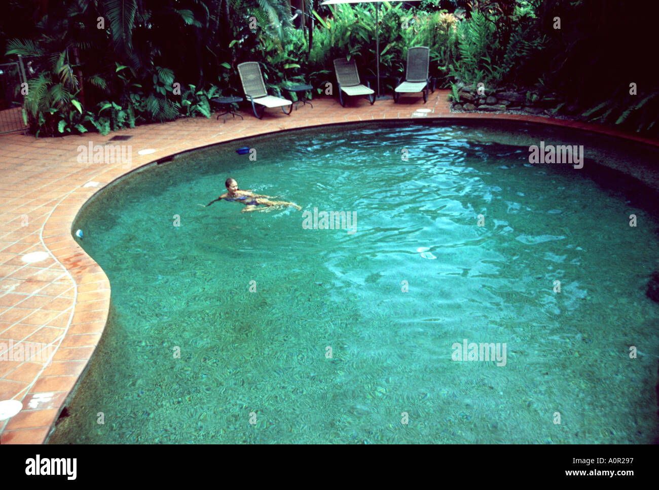 Swimming Pool in einem tropischen Ort mit jungen Frau, die in der Ferne schwimmen Stockfoto