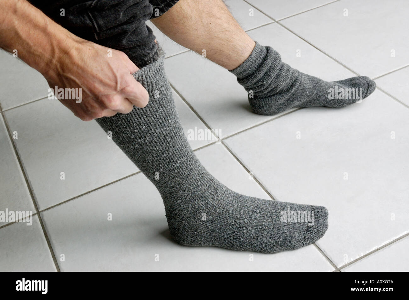 Man zieht sich seine Socken auf Fliesenboden Stockfoto