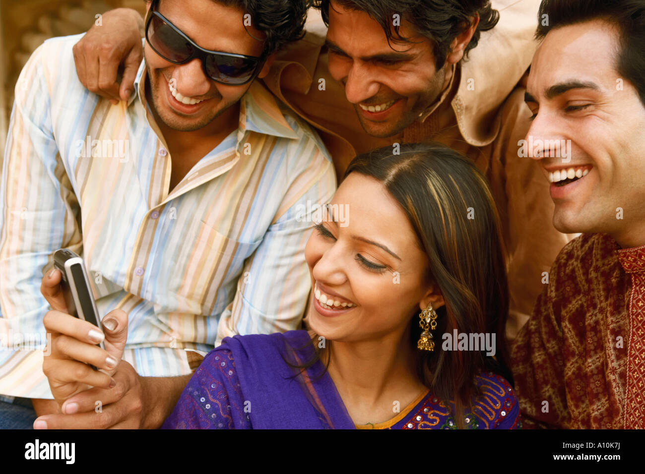 Nahaufnahme von drei junge Männer und eine junge Frau mit Blick auf ein Mobiltelefon und lächelnd, Agra, Uttar Pradesh, Indien Stockfoto