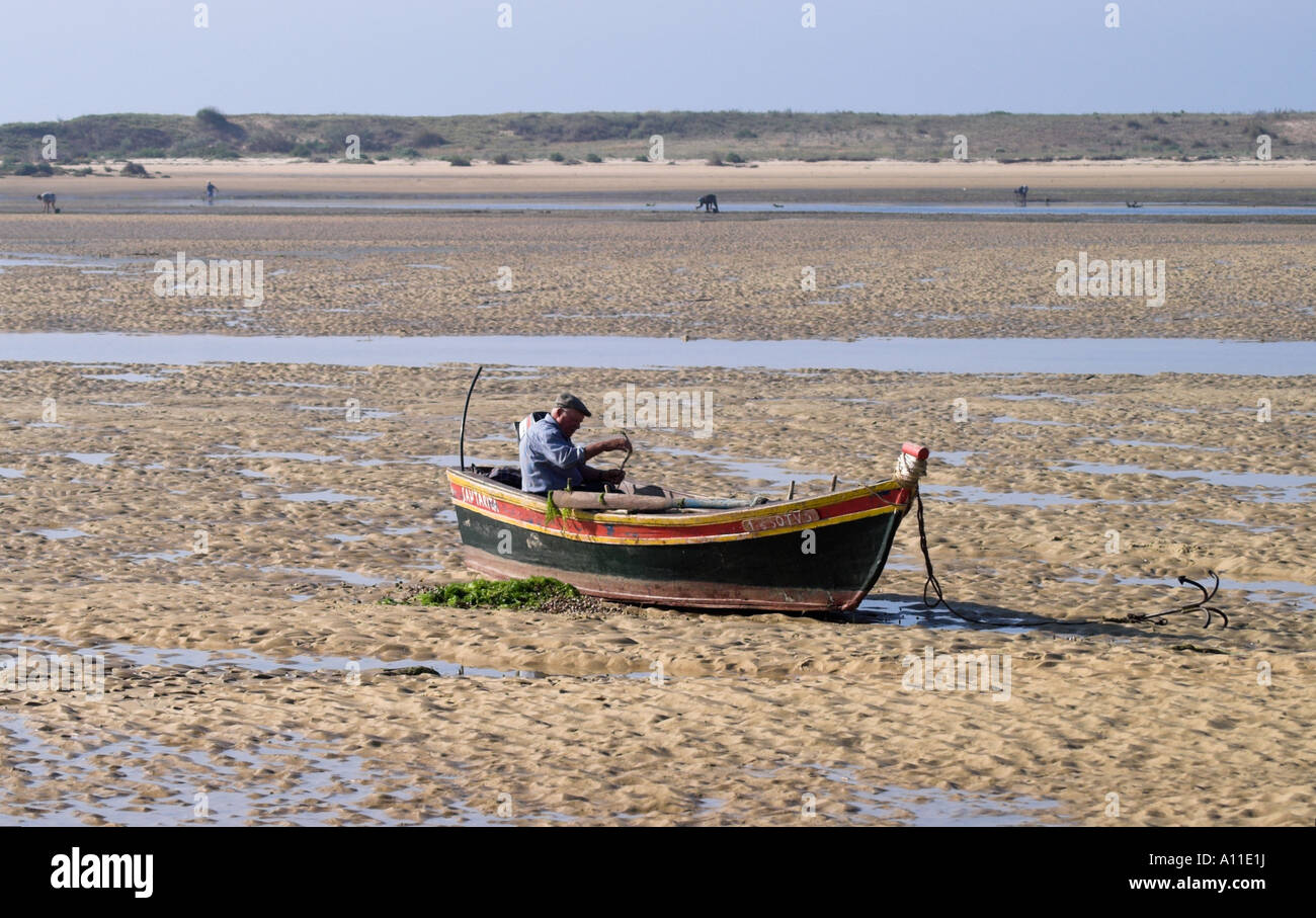 Ein Fischer sitzt in seinem Boot ausbessern seine Fanggeräte bei Ebbe an Ria Formosa, Algarve - Portugal Stockfoto