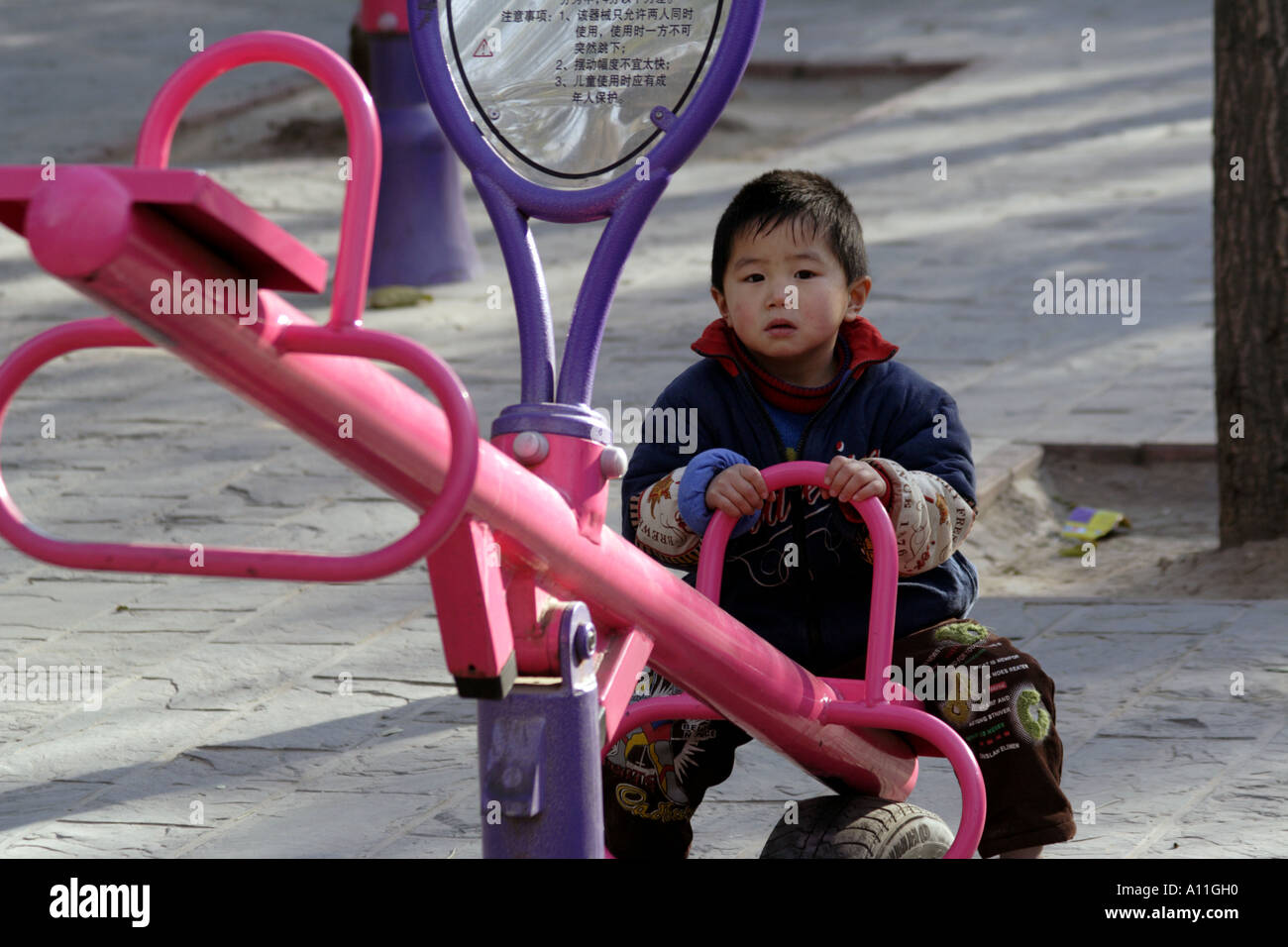 Chinesischen ein-Kind-Politik lässt dieser junge alleine auf einem Spielplatz Teeter Wanken, Dongdan Park, Peking, China Stockfoto