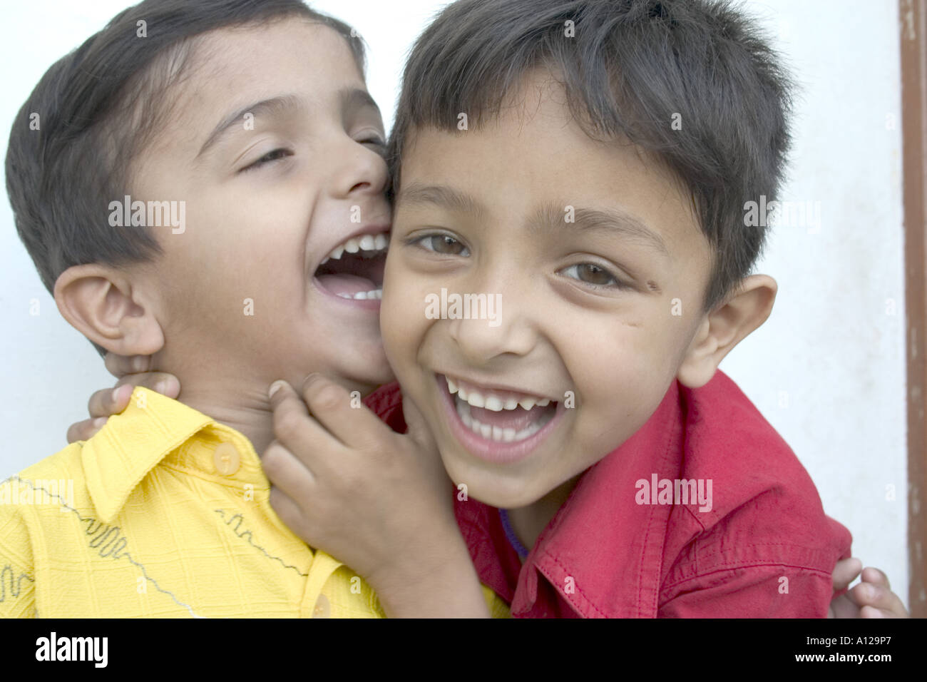 Zwei indischen jungen Kids Kinder Lächeln, lachen, spielen Scherz umarmt Spaß lustig teilen Witz glücklich Zähne Shirt rot, gelb Stockfoto