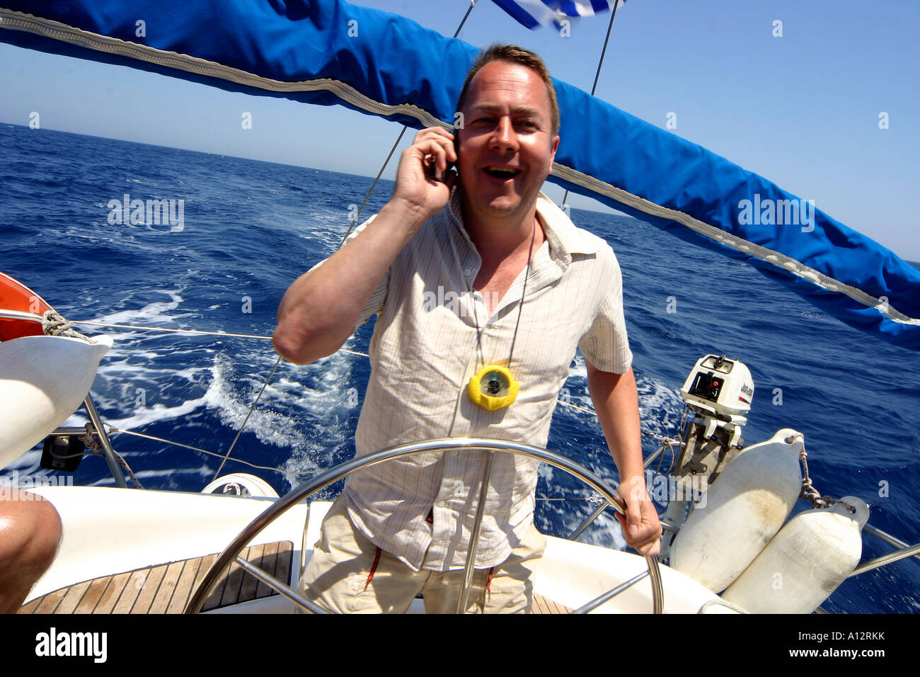 Mann in den dreißiger Jahren mit dem Handy telefonieren am Steuer einer Segelyacht in den griechischen Kykladen Stockfoto