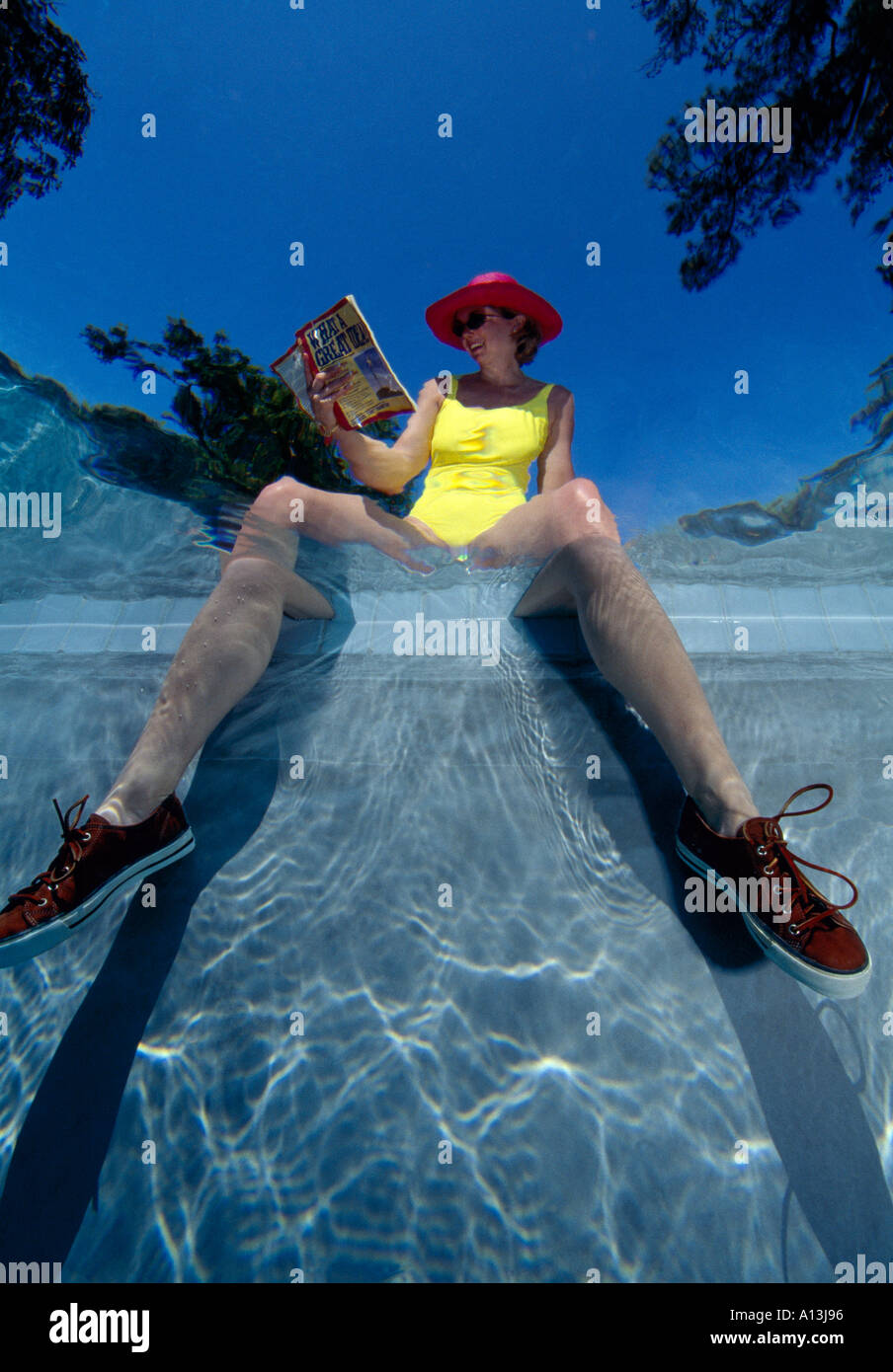 Frau im gelben Badeanzug Beine baumeln im Wasser mit Turnschuhen auf Füße aus dem Wasser genommen Stockfoto