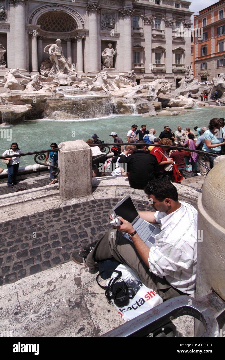 Historischer Trevi-Brunnen Statuen und Skulpturen Mann sitzt auf Pflaster mit Laptop-Computer mit Kamera in der Hand vermutlich Foto Rom Italien hochladen Stockfoto