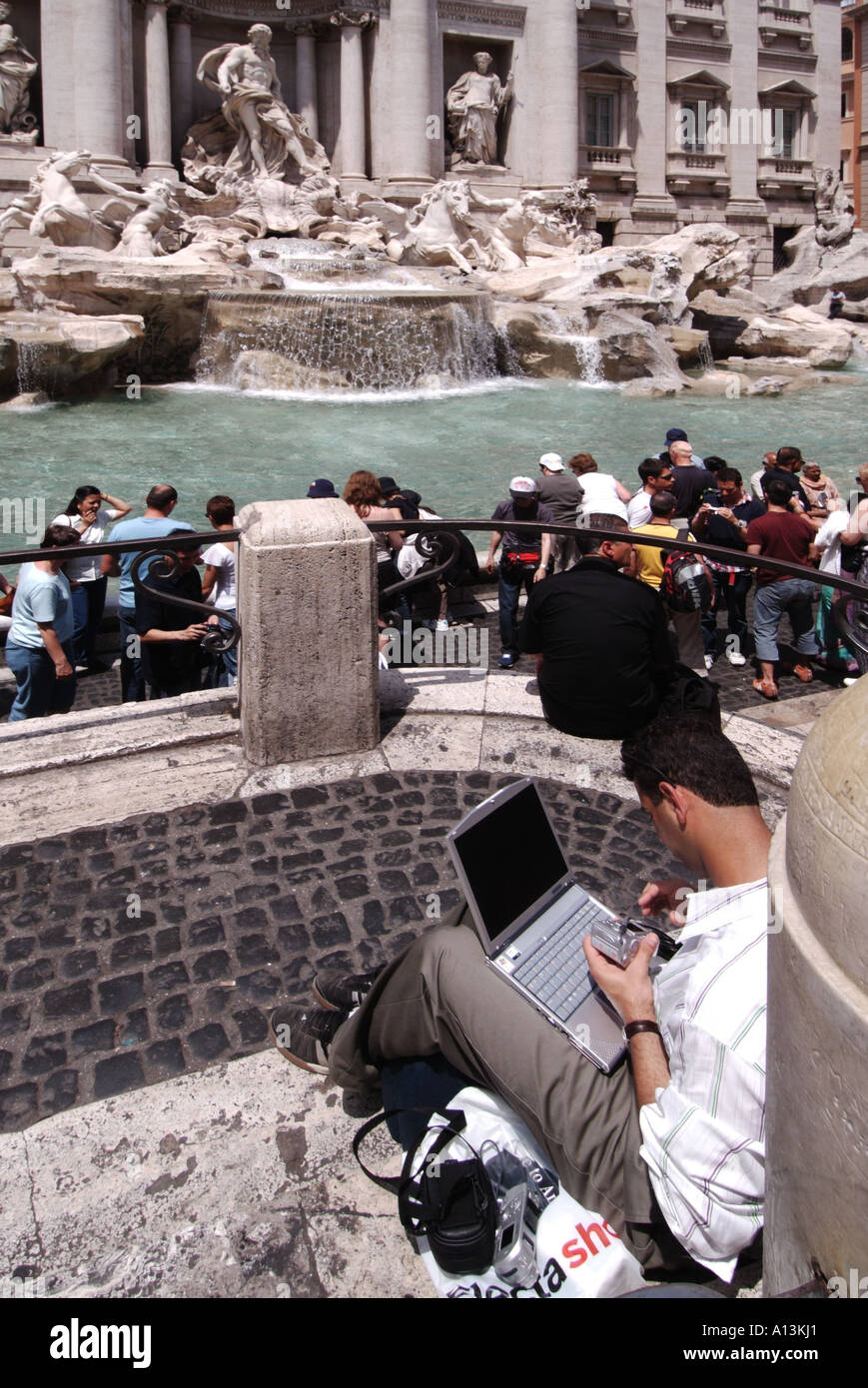 Historischer Trevi-Brunnen Statuen und Skulpturen Mann sitzt auf Pflaster mit Laptop-Computer mit Kamera in der Hand vermutlich Foto Rom Italien hochladen Stockfoto