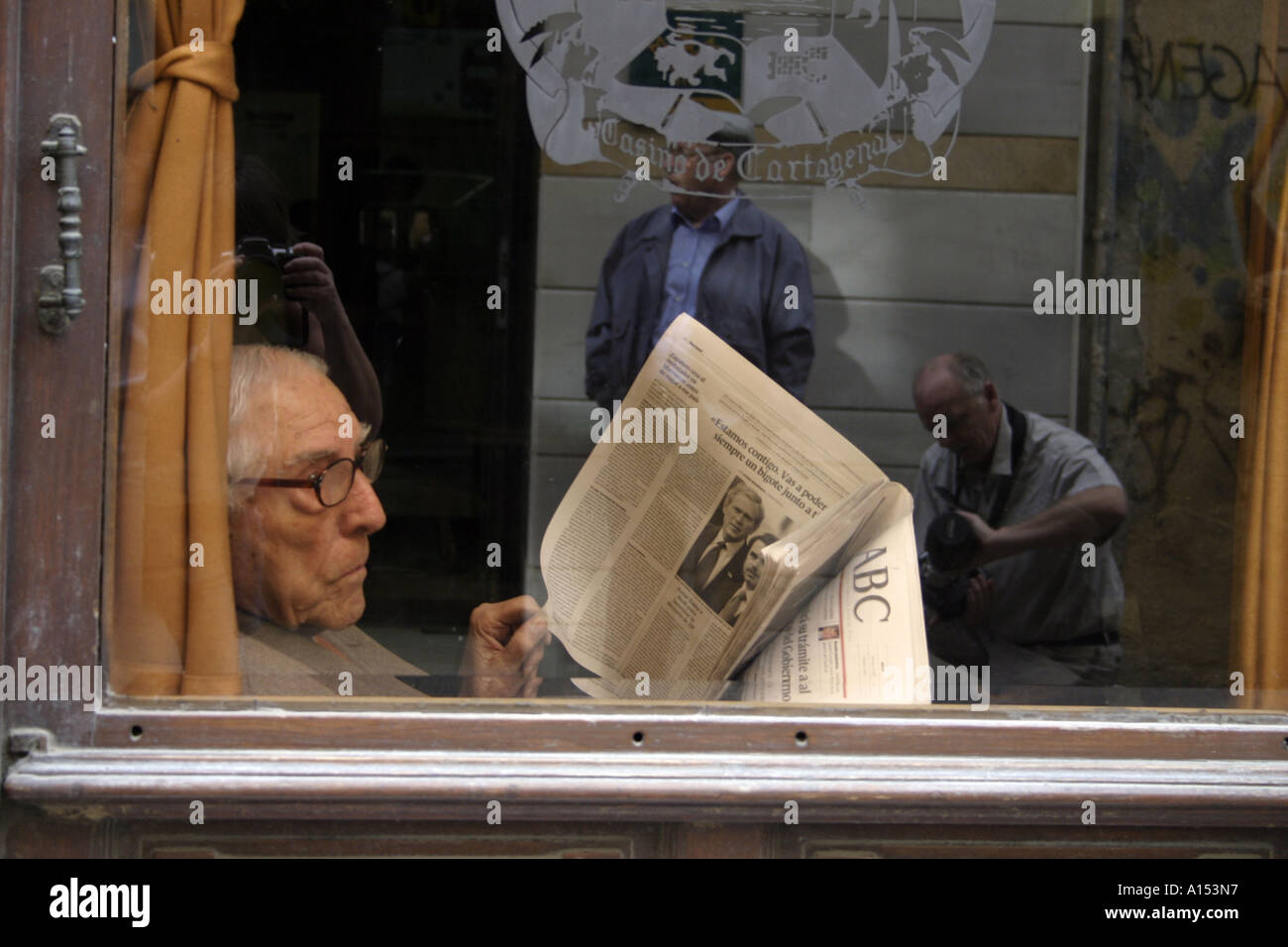 Älterer Herr, der Zeitung liest und auf das Straßenleben schaut In einem spanischen Café Stockfoto
