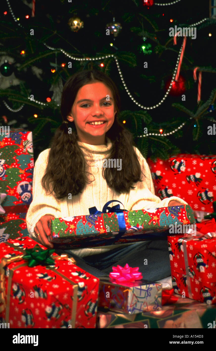 Porträt eines jungen Mädchens sitzen unter mehreren gewickelt Weihnachtsgeschenke vor einem Weihnachtsbaum Stockfoto