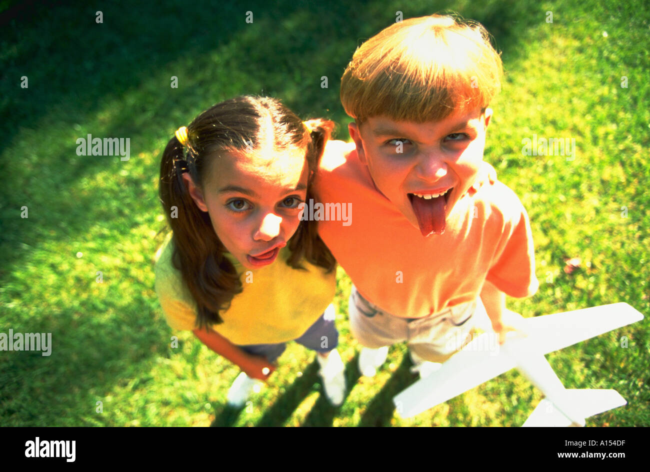 Luftaufnahme der ein Junge und ein Mädchen machen Gesichter in die Kamera halten Sie ein Modellflugzeug Stockfoto