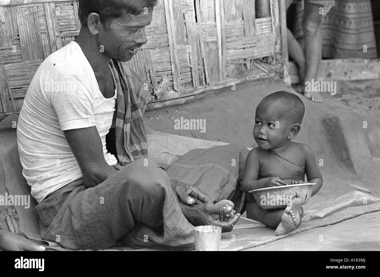 B/W eines Vaters mit seinem jungen Sohn, der zur Mealtime vor ihrem Dorfhaus saß. Nr.Jamalpur, Bangladesch Stockfoto