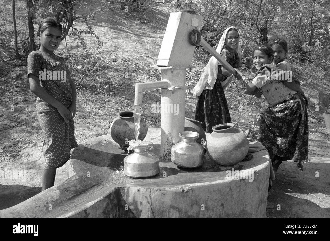 B/W einer Gruppe junger Mädchen, die Wasser in Metall- und Tontöpfe an einer Dorfwasserpumpe saugen. Tilonia, Rajasthan, Indien Stockfoto