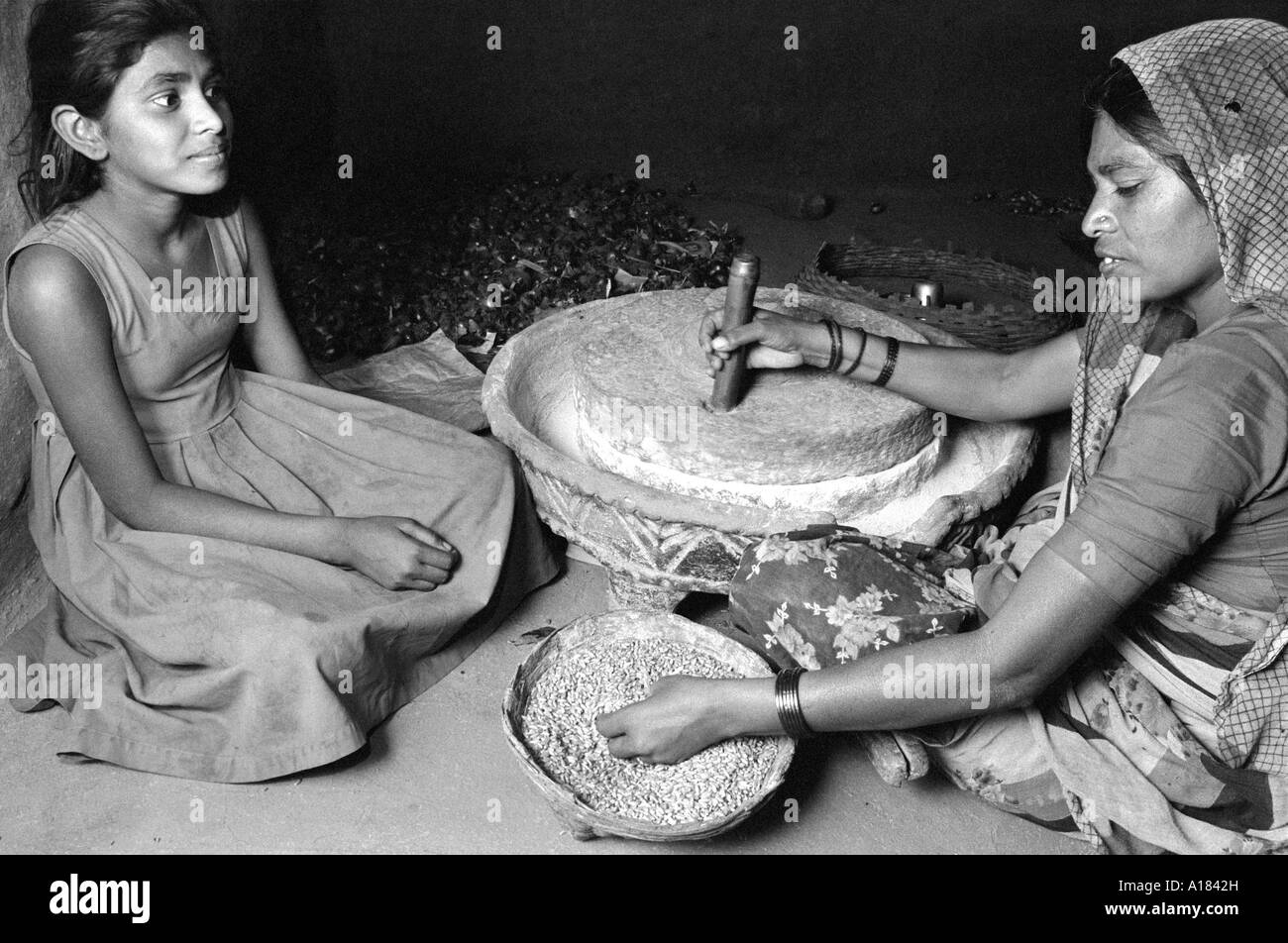 B/W von Mutter und Tochter zu Hause Mahlen auf traditionelle Weise zwischen zwei Schleifsteinen (Chakki) im ländlichen Gujarat, Indien Stockfoto