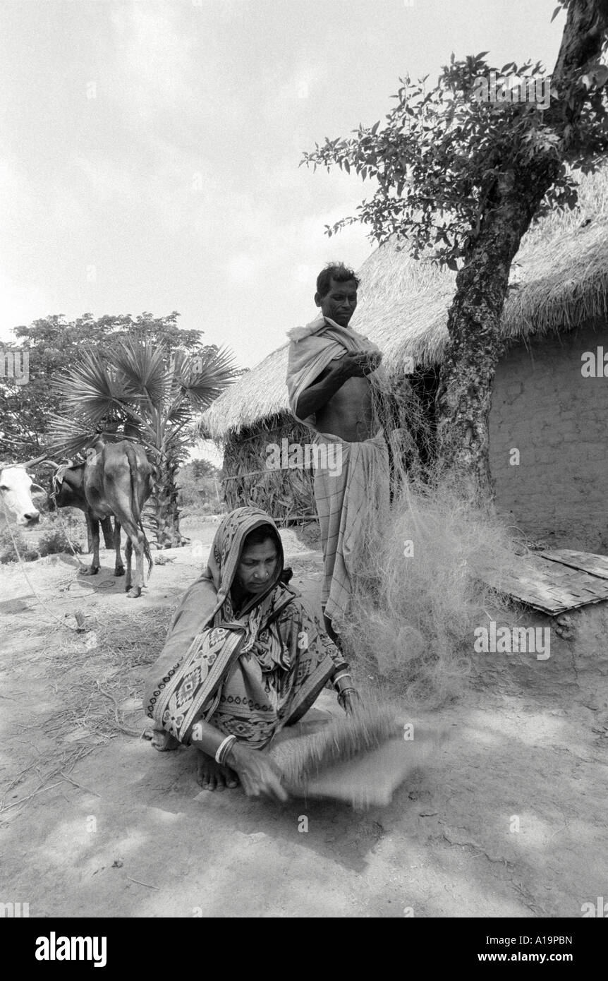S/W eines Fischers, der seine Netze ausbessern und seine Frau, die Reis vor ihrem Haus im ländlichen Odisha verschlungen hat. Indien Stockfoto