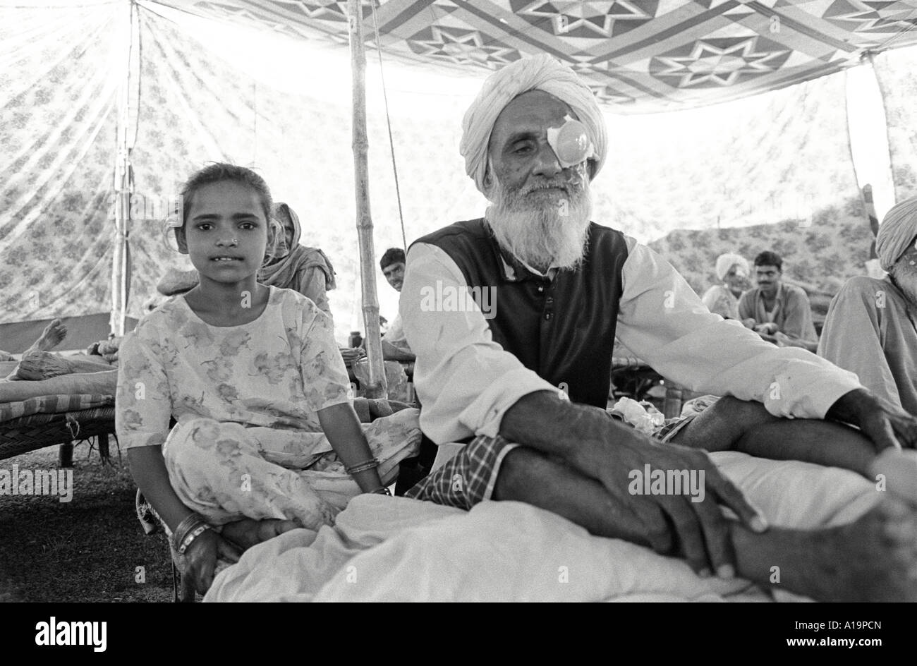 S/W eines älteren Mannes, der sich von einer Kataraktoperation in einem Zelt in einem Augenlager erholt, das von seiner Enkelin besucht wird. Rajasthan, Indien Stockfoto