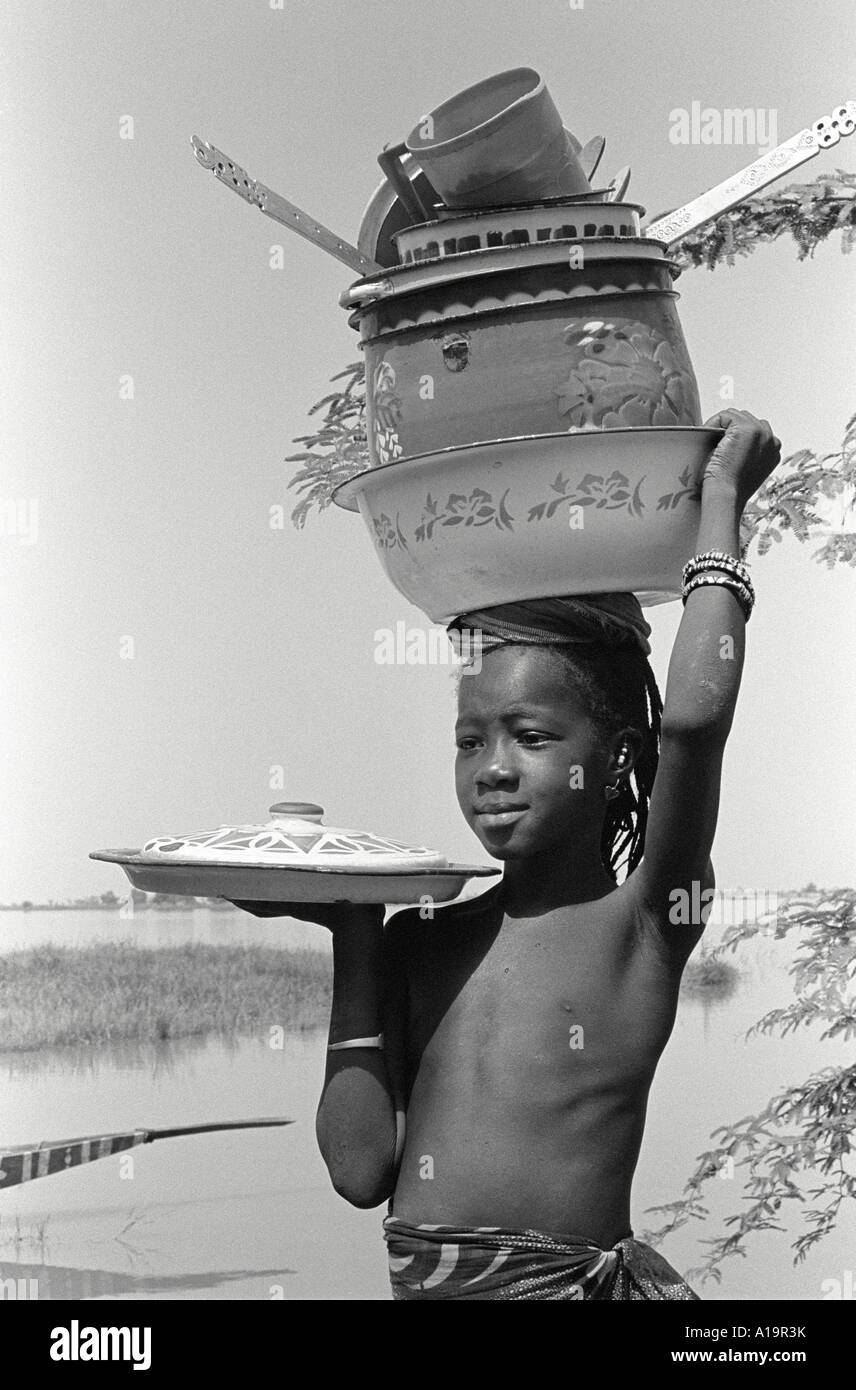 S/W eines jungen Mädchens aus dem Stamm der Bozo, das Küchentöpfe und Pfannen auf dem Kopf balanciert, Dagua Womina, Mali, Westafrika Stockfoto