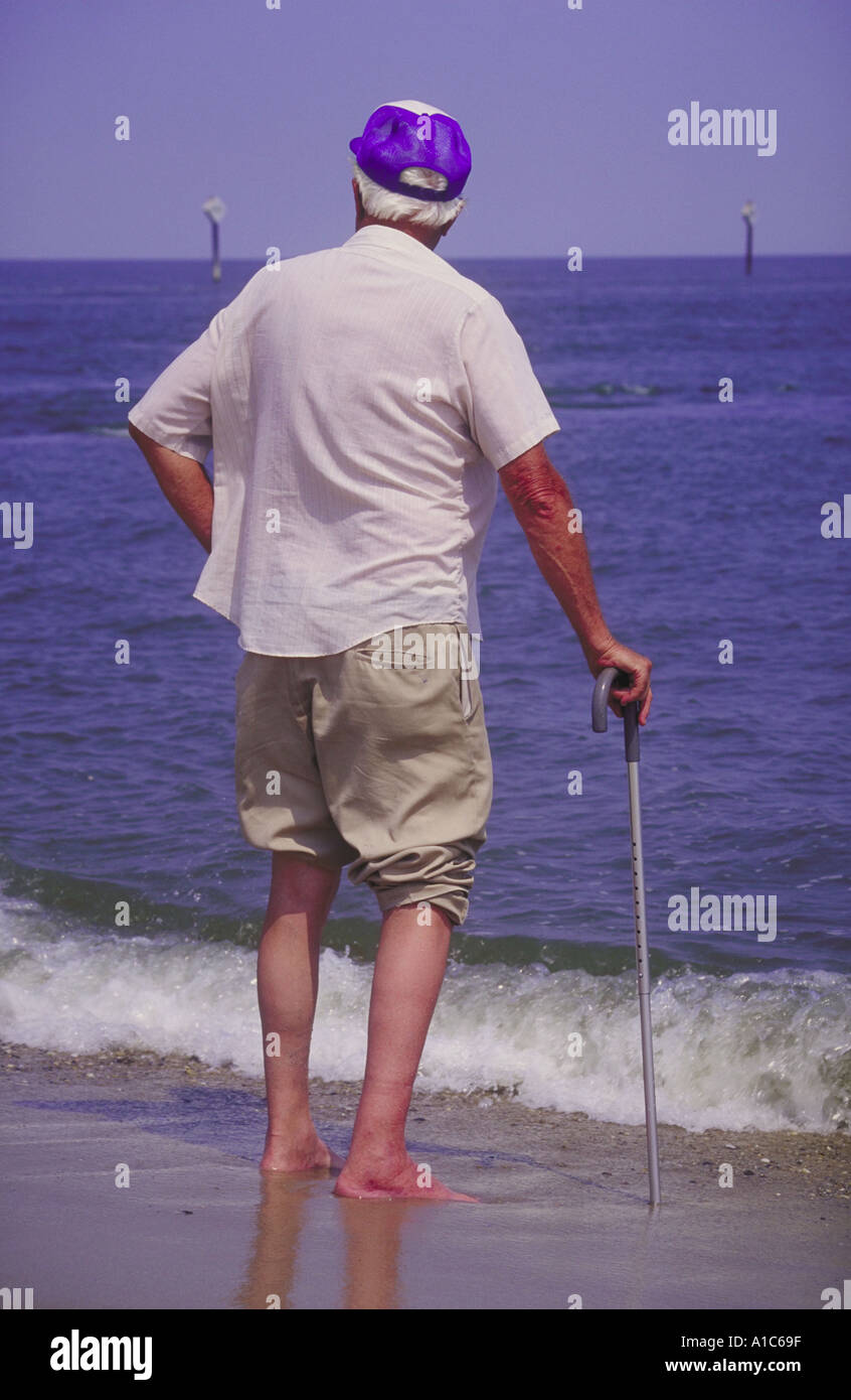 Ältere Mann allein Hand auf einen Gehstock mit abgerundeten Schultern stehend im Wasser Kante Blick bis zum Horizont Stockfoto