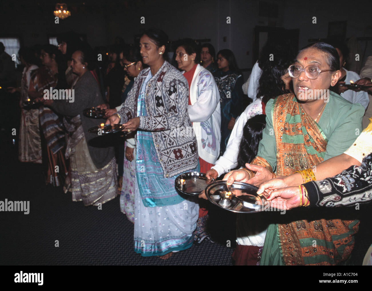 Hinduistische Frauen, die Arti durchführen, das Winken von beleuchteten Lampen vor einem Bild einer Gottheit oder einer Person, die geehrt werden soll. Stockfoto Hinduistische Frauen, die Arti durchführen, das Winken von beleuchteten Lampen vor einem Bild einer Gottheit oder einer Person, die geehrt werden soll. Stockfoto