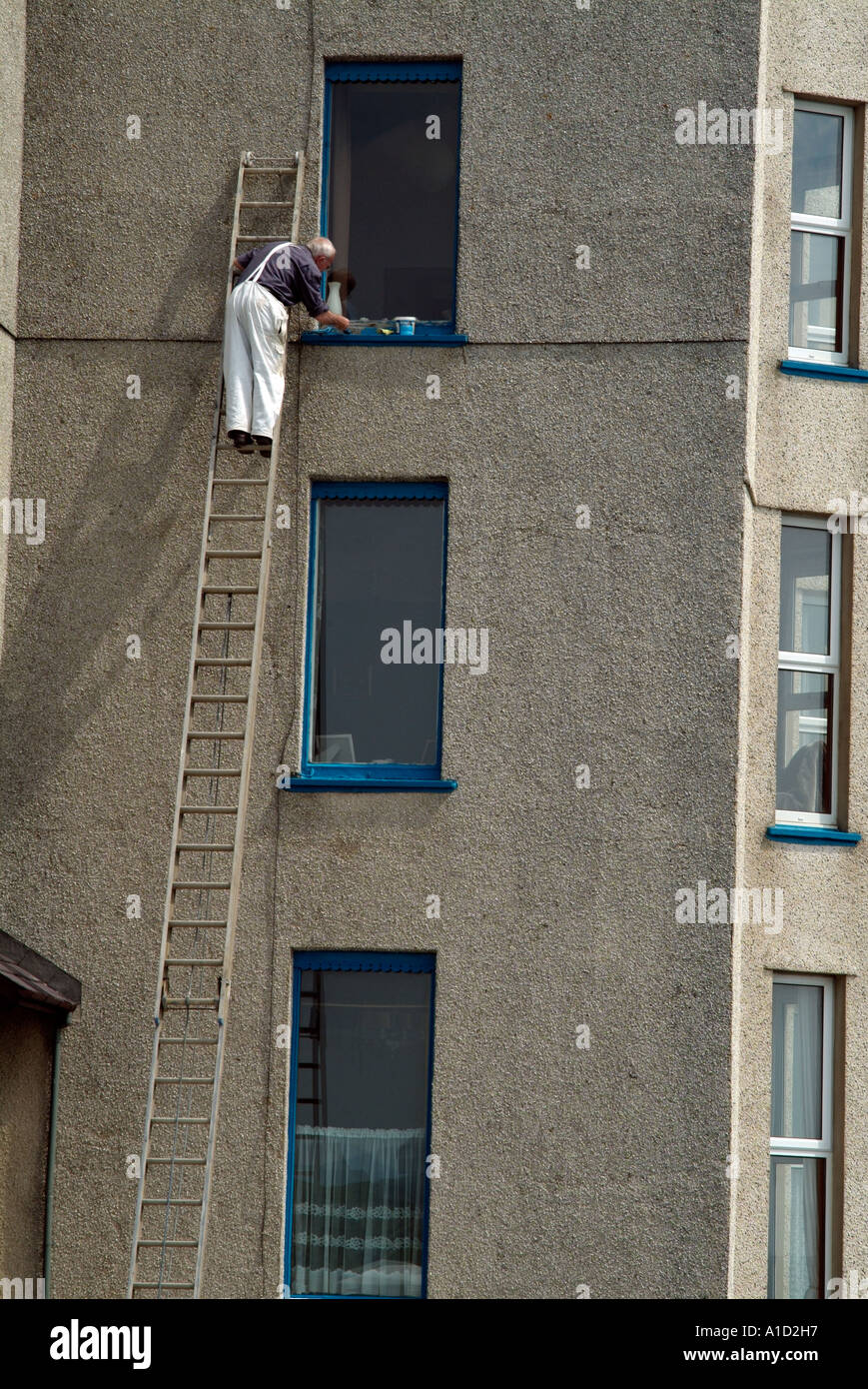 Mann malte Fenster auf einer sehr hohen Leiter, zeigt große Höhe und keine Angst Stockfoto