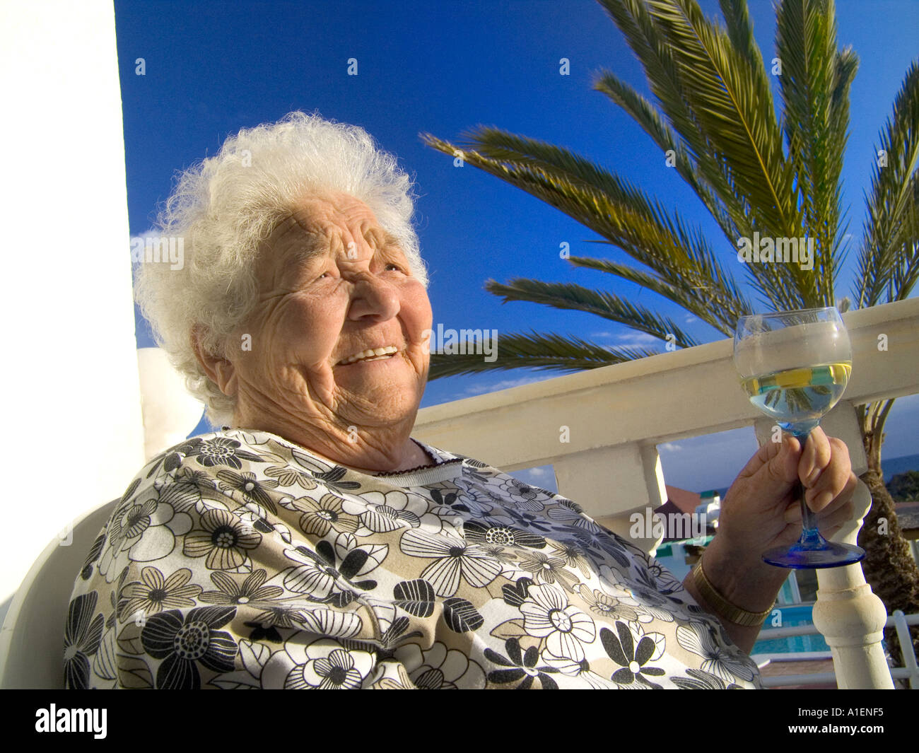 Ältere Frau entspannt zufrieden in der Sonne mit einem Glas Weißwein in ihrer Ferienvilla nach Hause Stockfoto