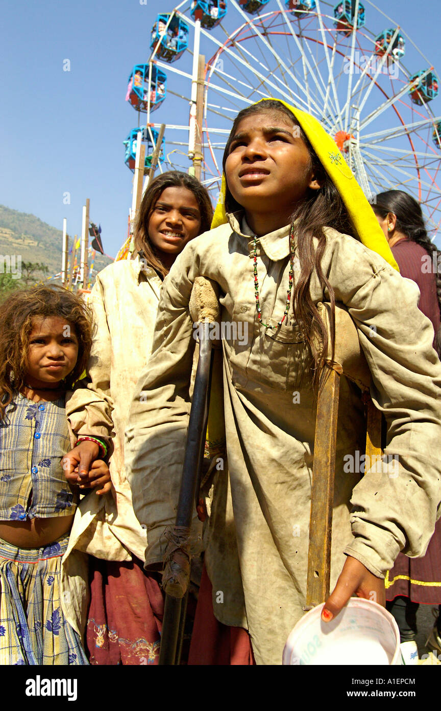 Drei junge Mädchen Kinder Bettler mit Krücke und Karussell Hintergrund Dussehra-Festival in Kullu, Indien Stockfoto