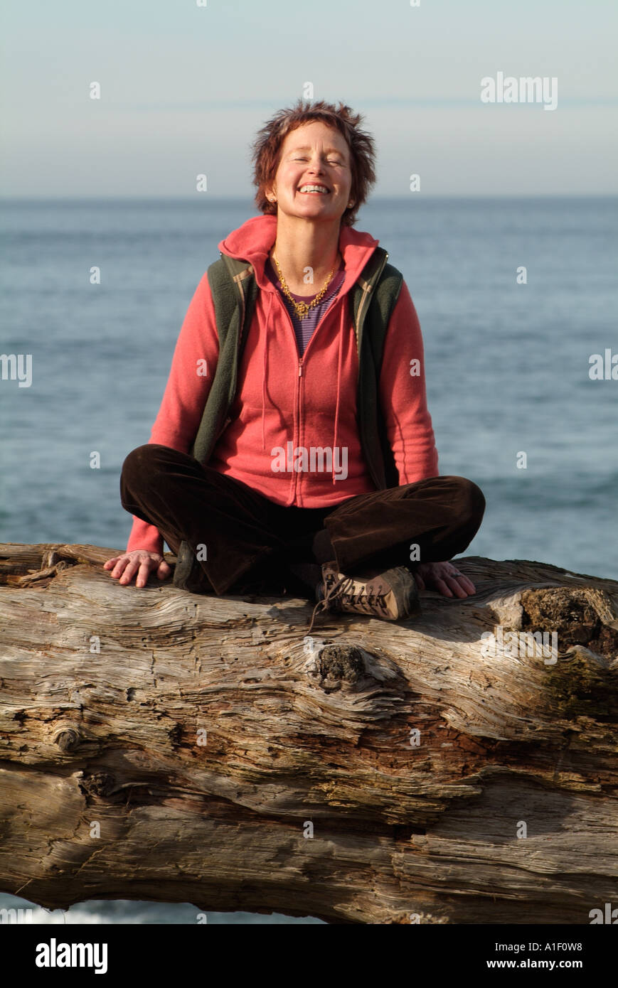 Frau auf Log am Strand, middle aged, mittleren Leben Schneidersitz sitzen, lachen Stockfoto