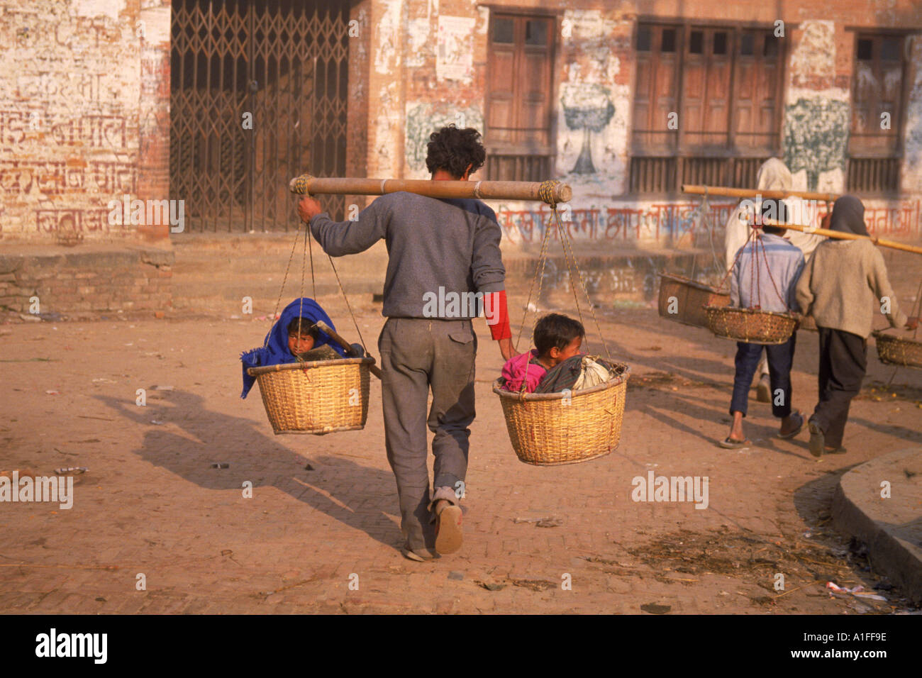 Kinder taxi zwei Kinder in Körben an einem Mast, durchgeführt von einem Mann in Bhaktapur Nepal Asien G Hellier durchgeführt Stockfoto