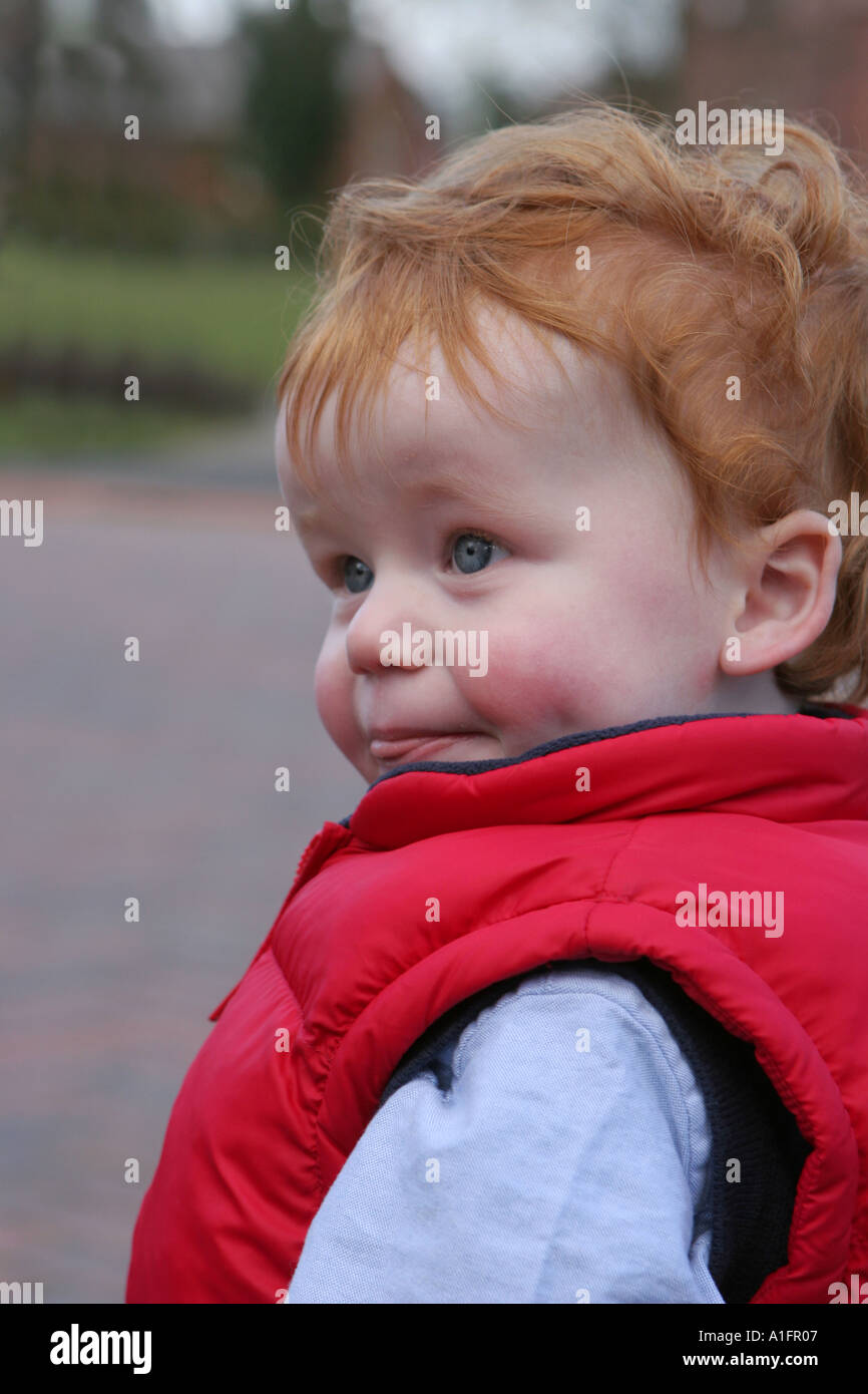 Baby mit roten Haaren tragen einen roten Körper wärmer draußen spielen Stockfoto