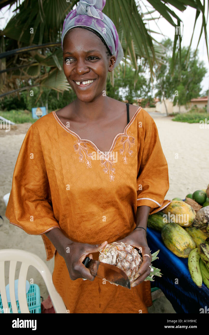 Frau Obstverkäufer in traditioneller Kleidung schält Ananas The Cape Beach Bakau Gambia Stockfoto