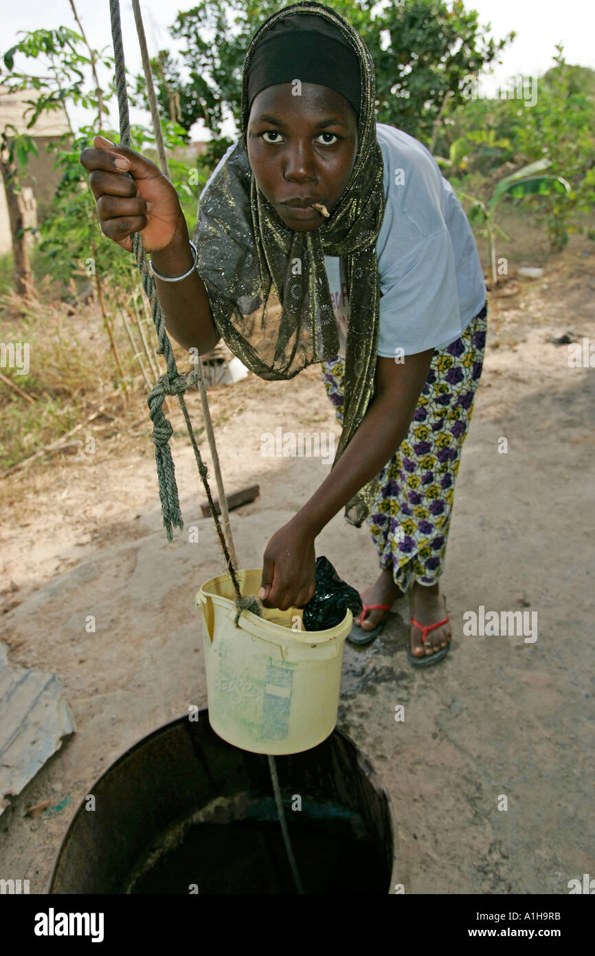 Fula Frau zieht Wasser aus Brunnen in Plastikeimer Gambia Stockfoto