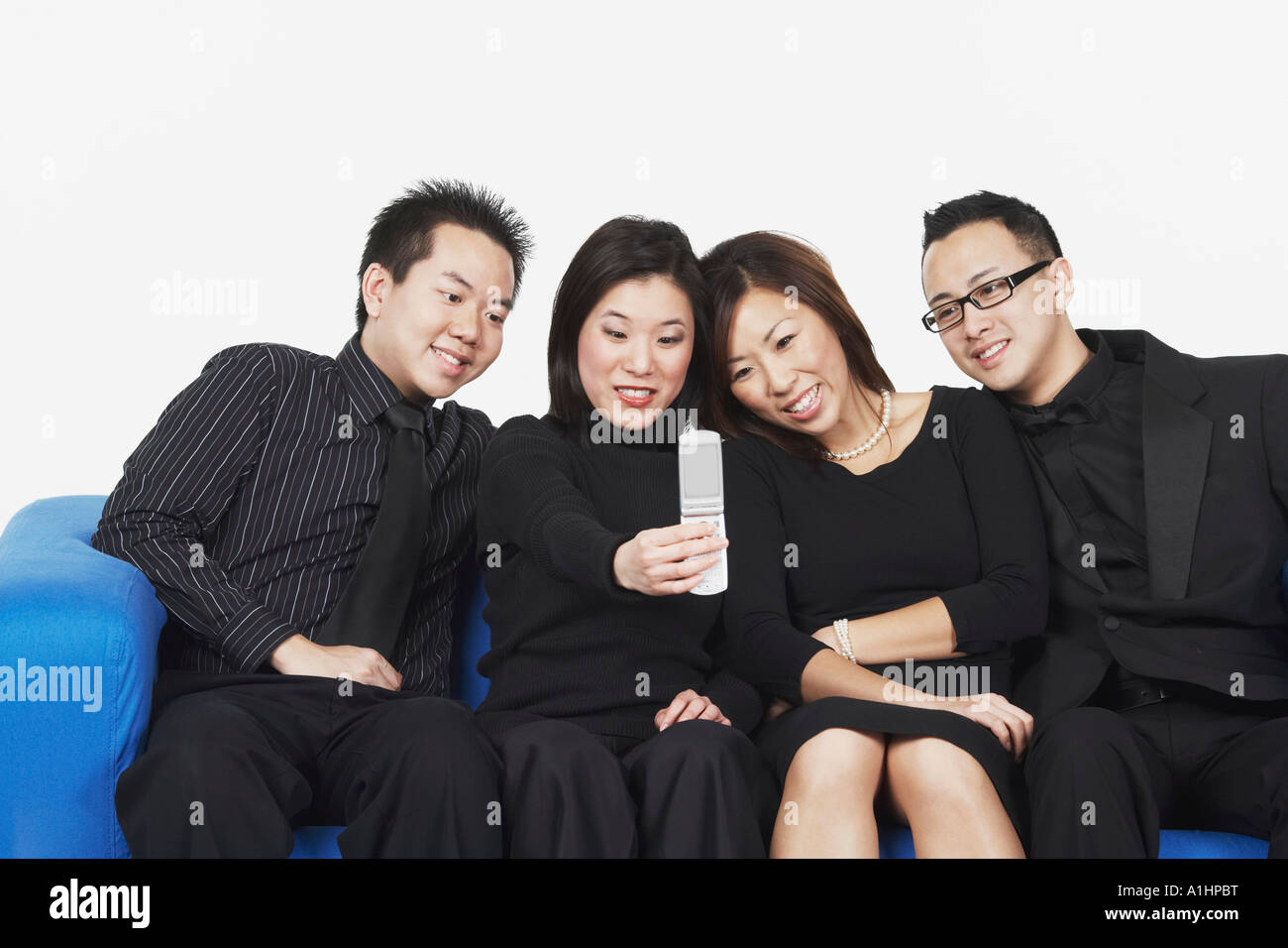 Zwei junge Männer und zwei junge Frauen sitzen auf einer Couch, Blick auf ein Mobiltelefon Stockfoto