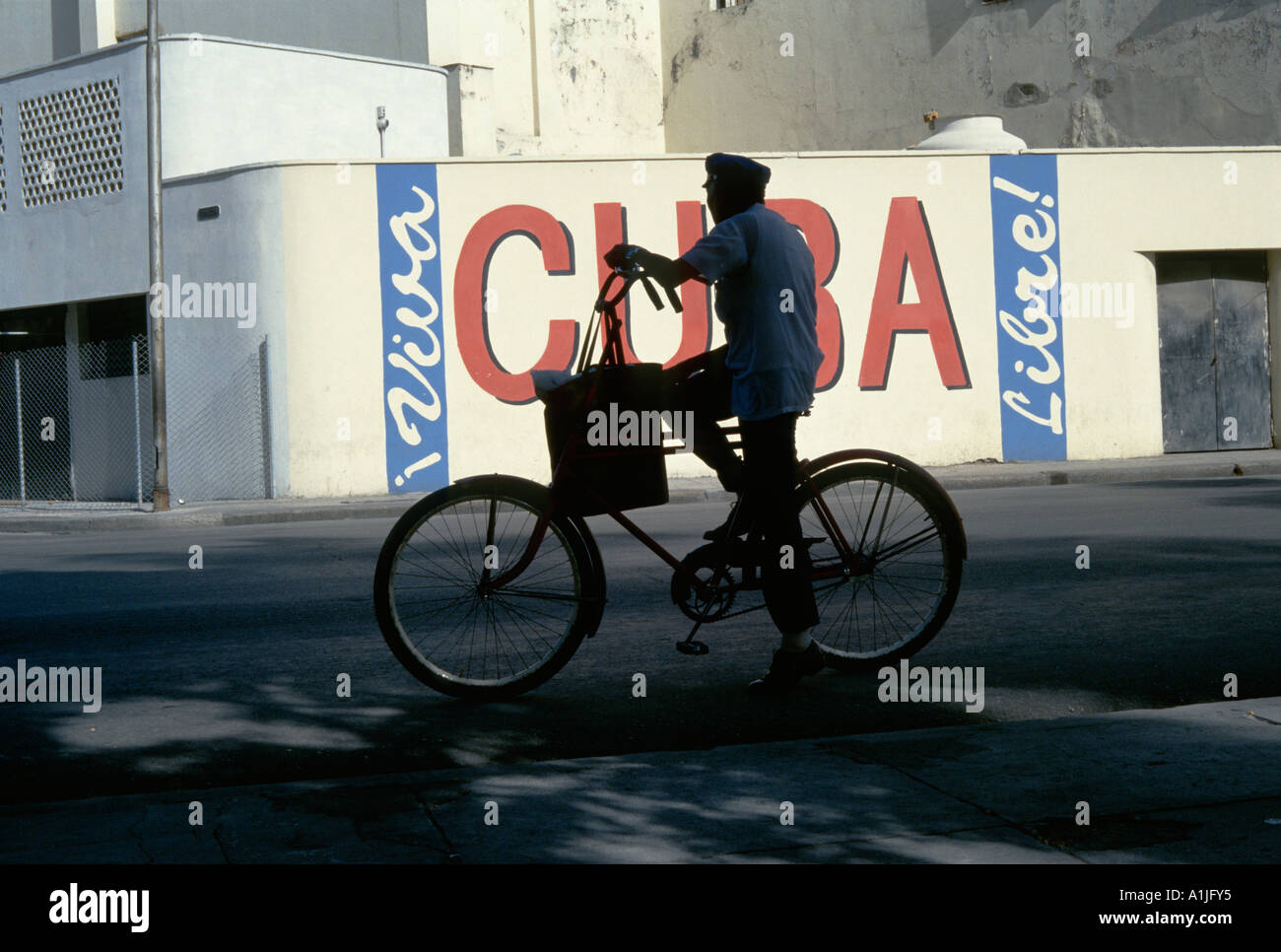 Havanna-Kuba-Mann auf einem Fahrrad mit revolutionären Parolen im Hintergrund Stockfoto