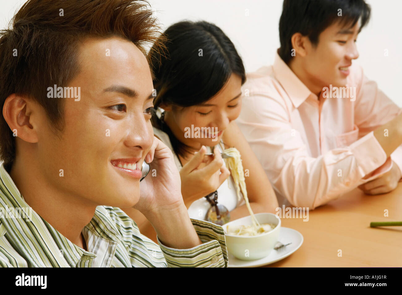Nahaufnahme eines jungen Mannes mit ein junges Paar sitzt neben ihm auf dem Handy zu reden Stockfoto