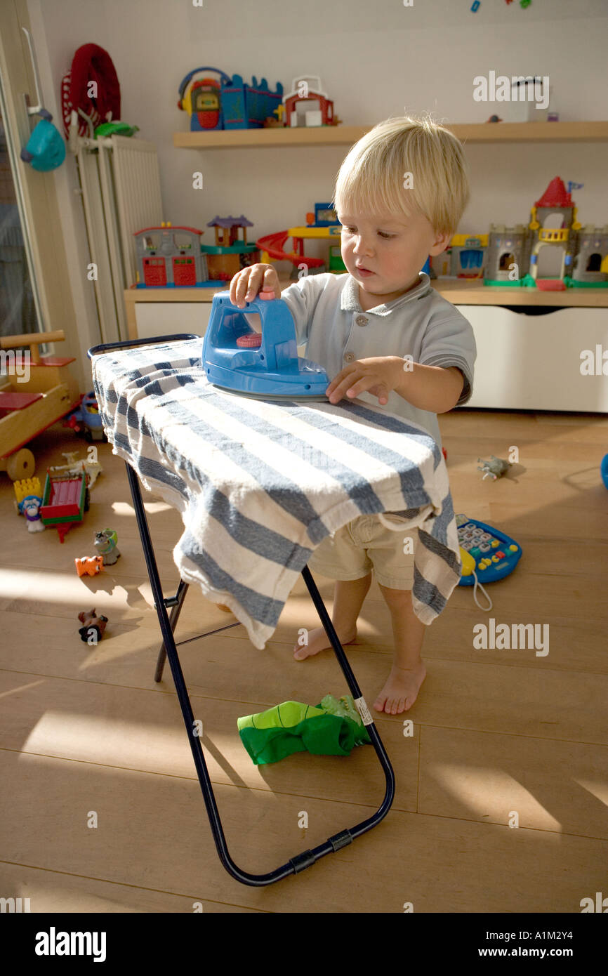 Ein Litlle blonder Junge in einer Kindertagesstätte spielen mit Bügeleisen und Bügelbrett Stockfoto