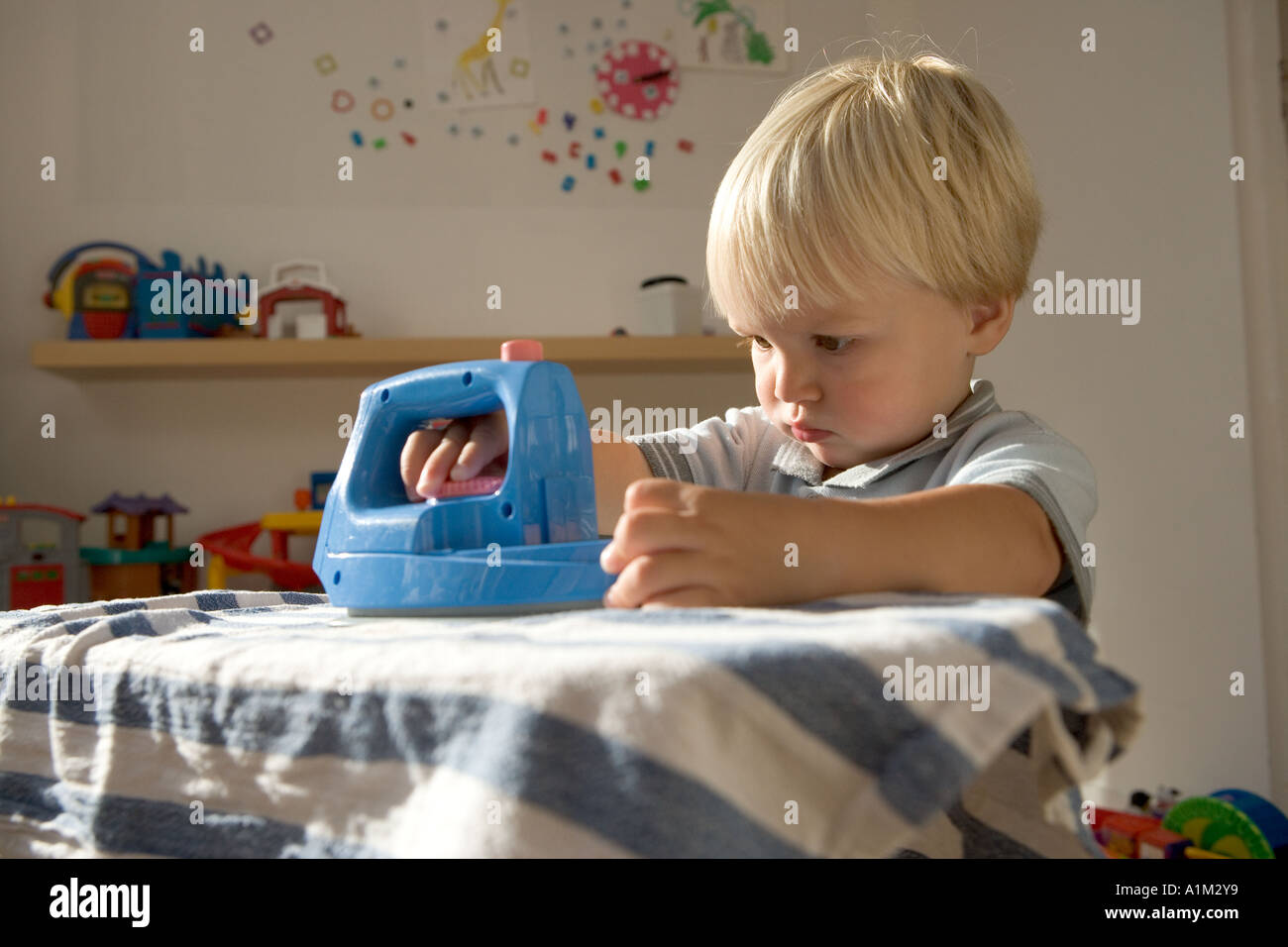 Ein Litlle blonder Junge in einer Kindertagesstätte spielen mit Bügeleisen und Bügelbrett Stockfoto