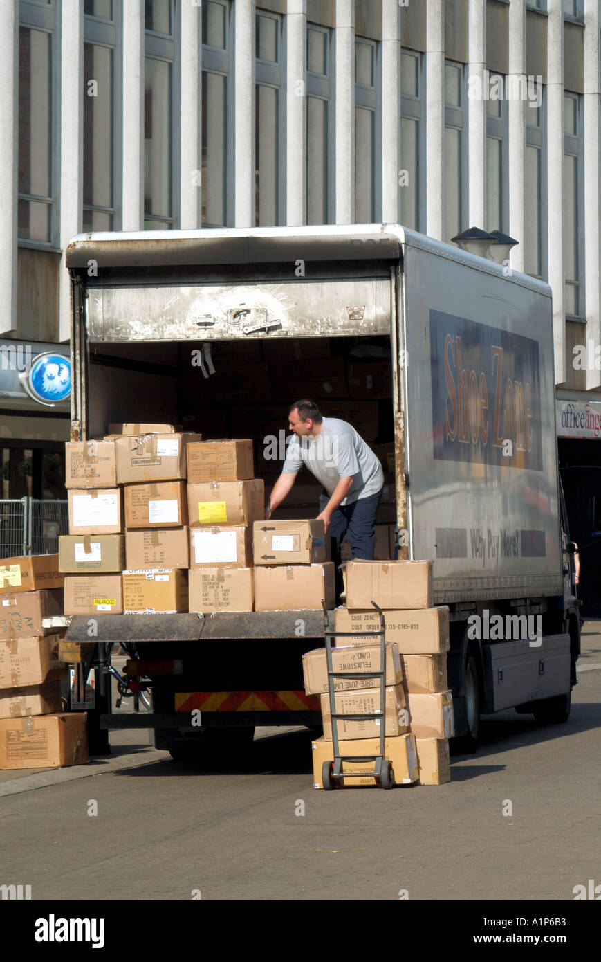 Rückansicht LKW-Fahrer in Fußgängerzonen Entladen von Kartons mit Schuhen auf den Wagen zur Lieferung an den Shoe Zone Shop Peterborough UK Stockfoto