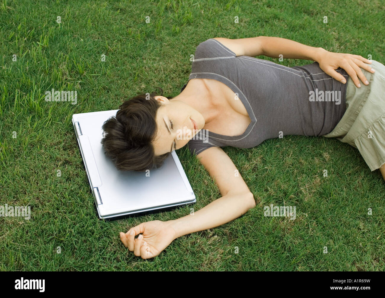 Frau liegend auf Rasen, Kopf ruht auf Laptop-computer Stockfoto
