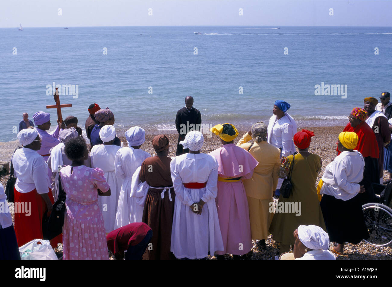CHRISTLICHE TAUFE ZEREMONIE STATT IM MEER IN BRIGHTON MENSCHEN IN BUNTEN GEWÄNDERN SAMMELN AM STRAND GEKLEIDET Stockfoto