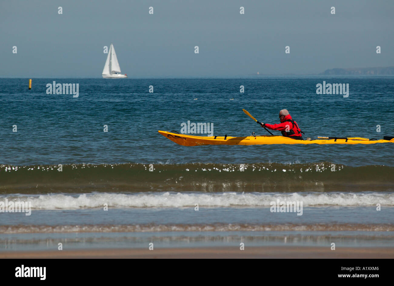 Gelben Kanu mit Mann Rudern in rote Jacke, Segeln in der Nähe von schottischen Küste mit Yacht im Hintergrund Stockfoto