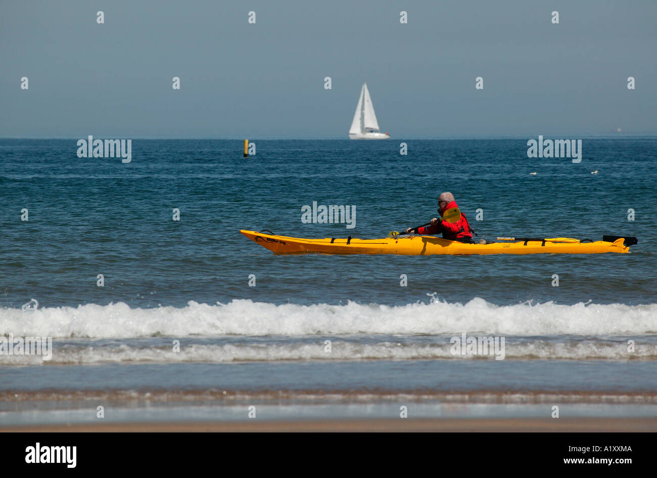 Gelben Kanu mit Mann in rote Jacke Segeln, nahe der schottischen Küste mit Yacht im Hintergrund Stockfoto