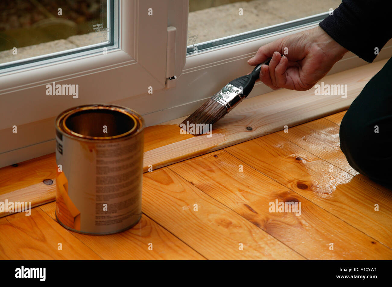Person, die die hölzernen Einfassung einer PVC-Tür mit einem Lack Pinsel und Dose Lack Lackieren Stockfoto