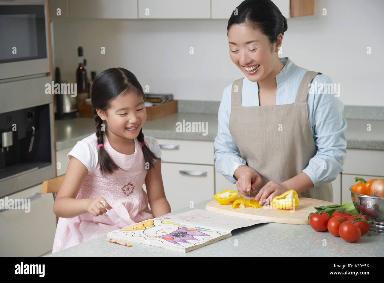 Tochter Färbung auf der Küchentheke, Mutter schneiden Paprika und beobachten Stockfoto