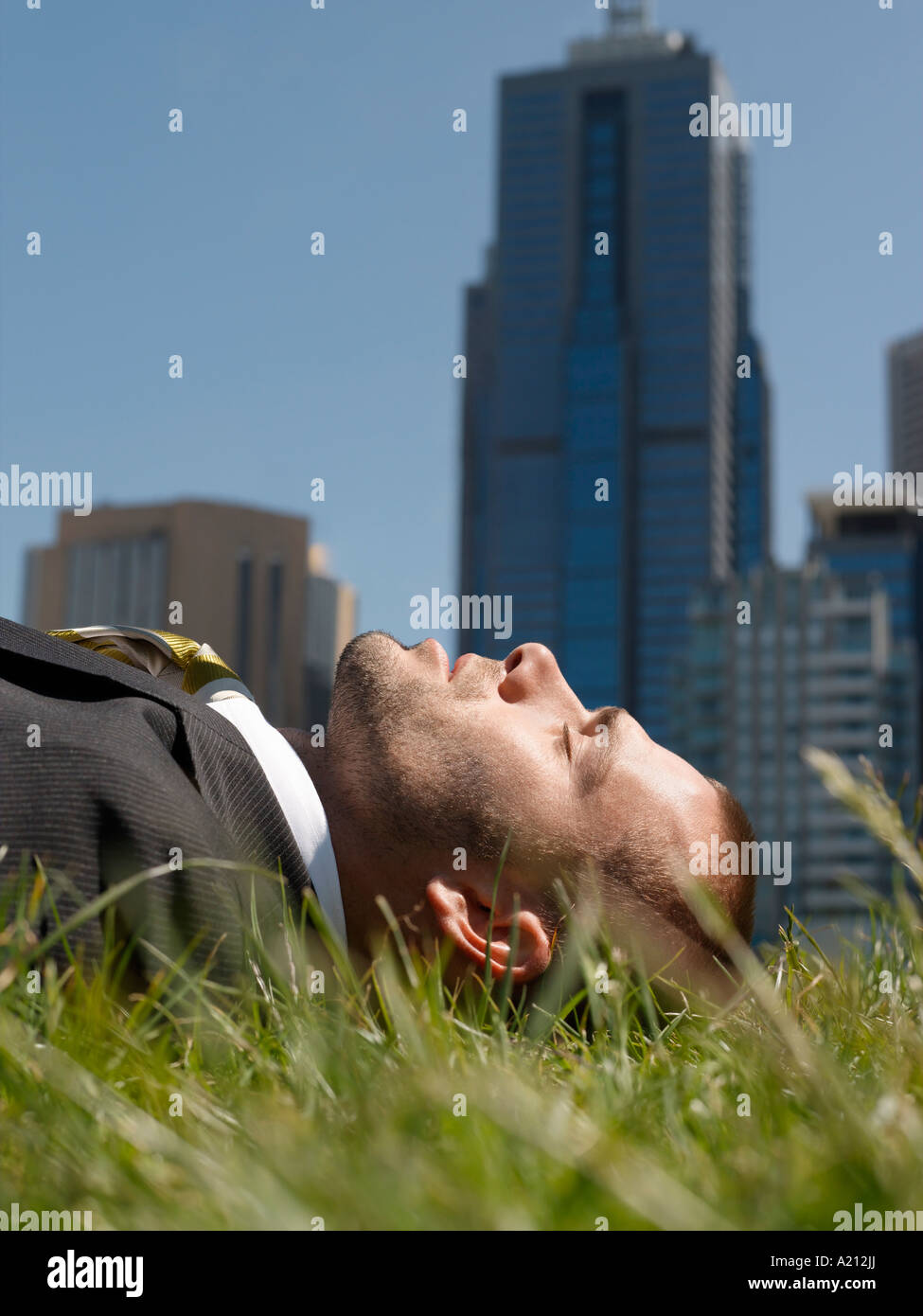 Business-Mann liegt auf dem Rasen, Bürogebäude im Hintergrund Stockfoto