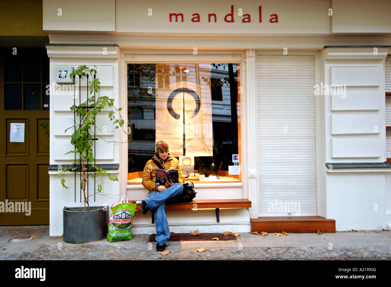 Eine junge Mand ein Buch auf einer Bank vor Geschäft auf Husemannstraße im Ost-Berliner Bezirk Mitte. Stockfoto