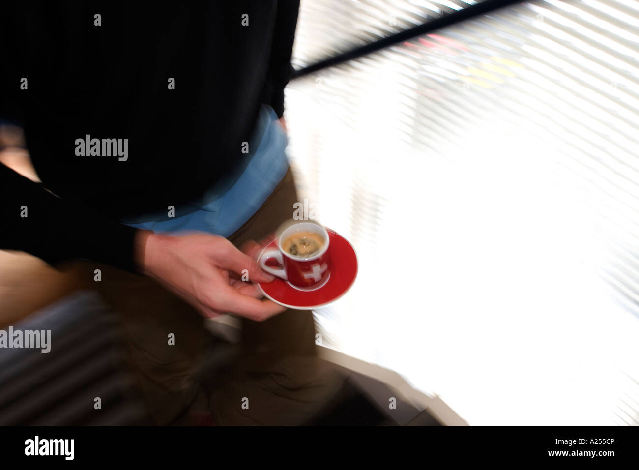 Ein Büroangestellter klettert Treppen zurück zu seinem Schreibtisch in einer Unschärfe mit einem Espresso in einer roten Schweizer Tasse und Untertasse. Stockfoto