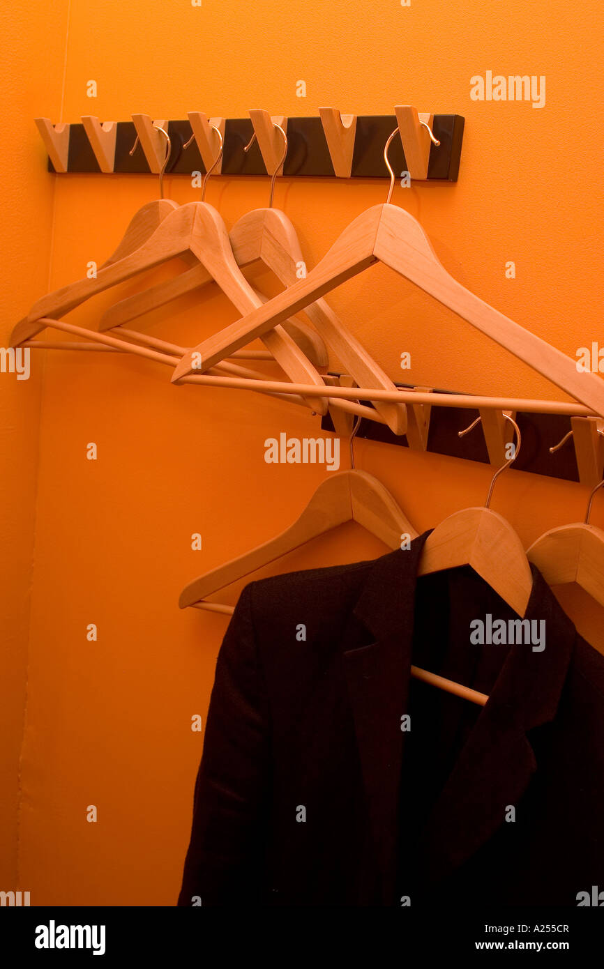 Eine Jacke hängt an orange Bürowand umgeben von nicht verwendeten Kleiderbügel Stockfoto
