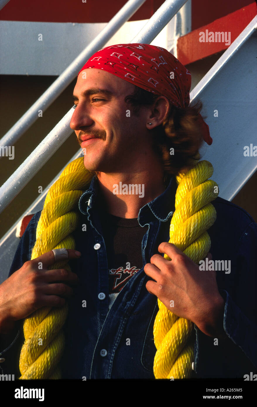 Profilbildnis einer amüsiert schnauzbärtige Deck Hand tragen in ein rotes Halstuch posiert mit einem dicken Abschnitt der hellen gelben Seil. Stockfoto