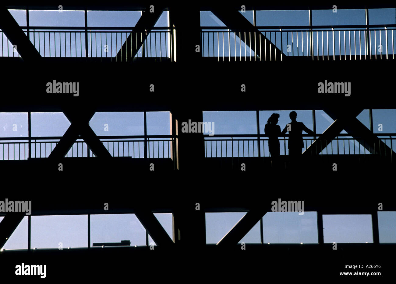 2 beleuchtete Menschen diskutieren die Ereignisse des Tages auf einem Steg in einem großen Unternehmen Hochhaus. Stockfoto