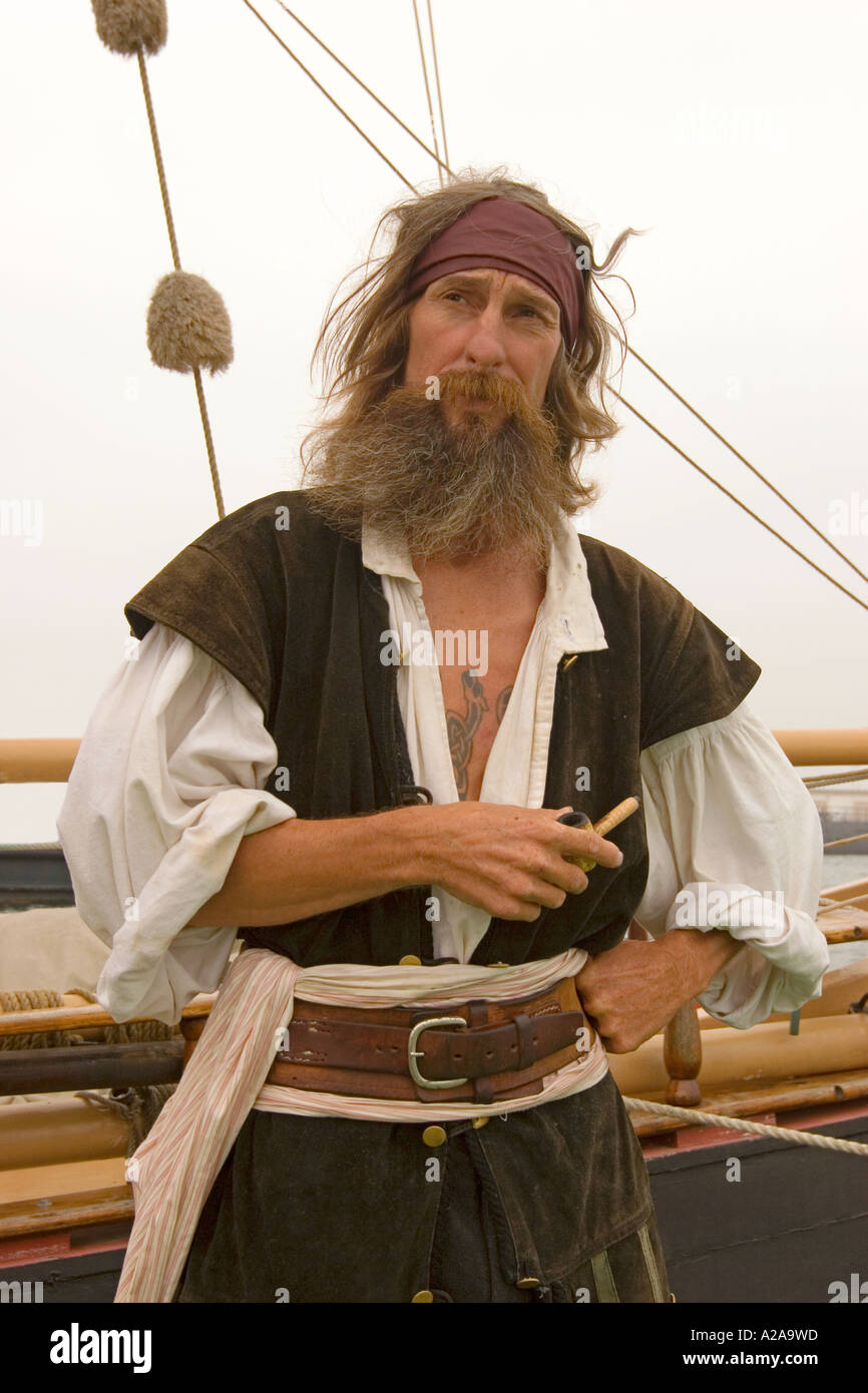Ein bärtiger Pirat steht man vor einem Segelschiff, hält seine Pfeife. Stockfoto